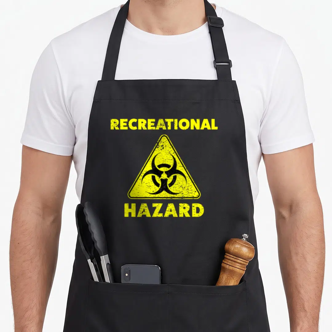 Recreational kickball apron - Yellow biohazard triangle with RECREATIONAL HAZARD text in distressed font — shown on a black cotton canvas apron against a white background