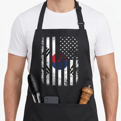 South korean american flag apron - Distressed composite flag with vertical stripes, red blue circle, black trigrams — shown on a black cotton canvas apron against a white background