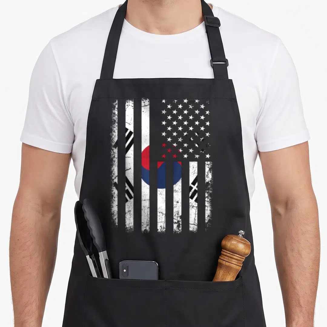 South korean american flag apron - Distressed composite flag with vertical stripes, red blue circle, black trigrams — shown on a black cotton canvas apron against a white background