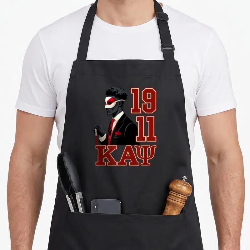 Funny psi alpha apron - Man in suit and mask with 1911 and KAPSI text in red and black — shown on a black cotton canvas apron against a white background