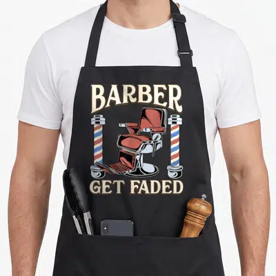 Faded hairdresser barber apron - Retro barber chair between two red blue and cream striped poles with arched text — shown on a black cotton canvas apron against a white background