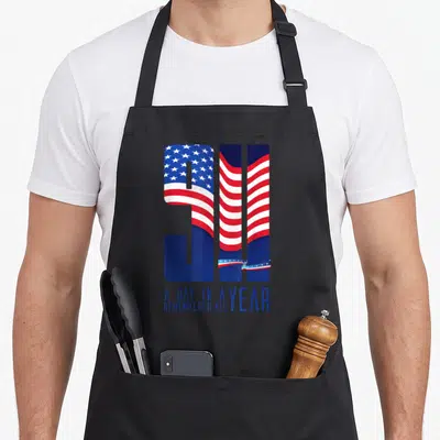 Memorial tribute apron - 911 numerals filled with waving US flag pattern above text A day in a year remembered all — shown on a black cotton canvas apron against a white background
