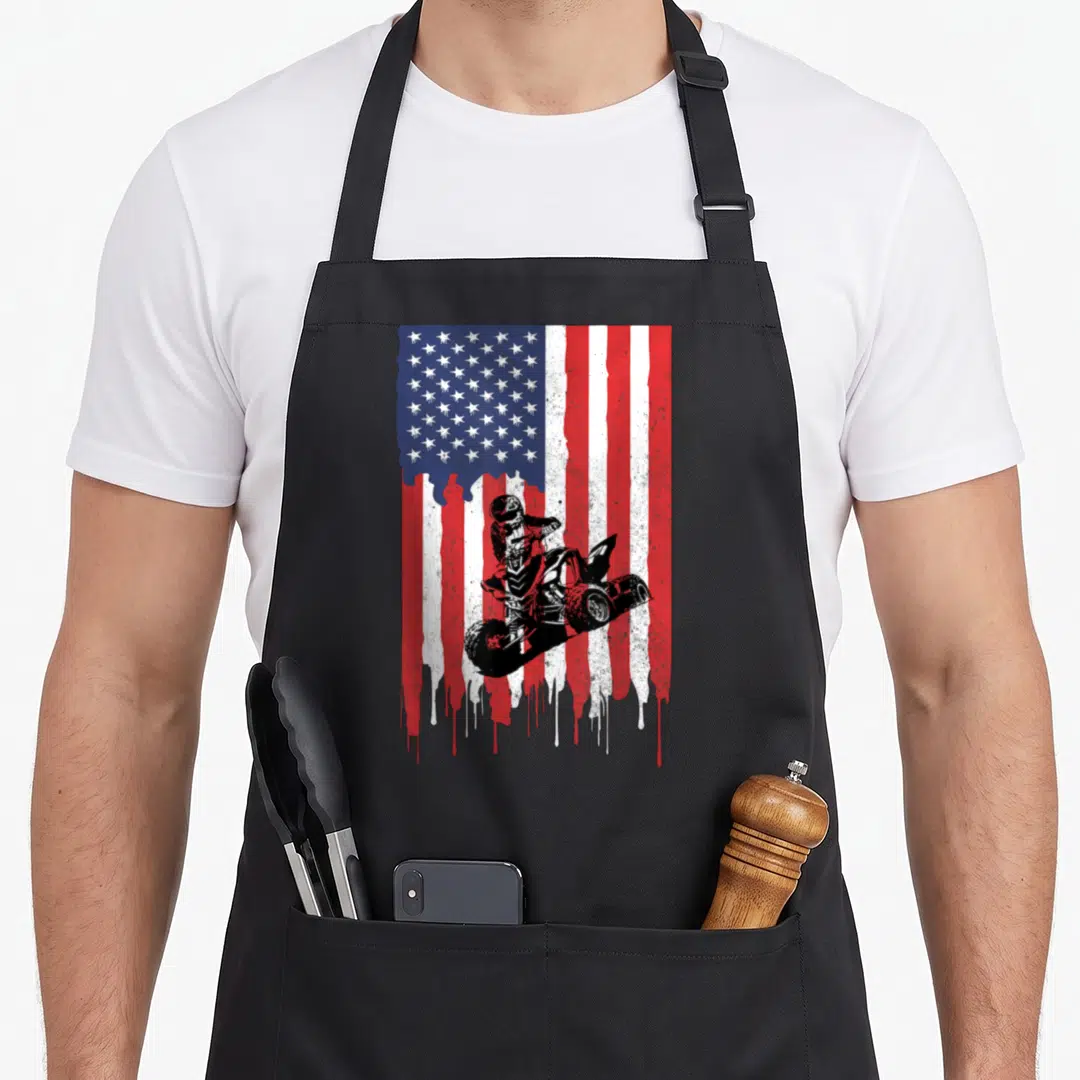 Atv four american flag apron - Black ATV rider jumping over distressed dripping red white blue USA flag design — shown on a black cotton canvas apron against a white background