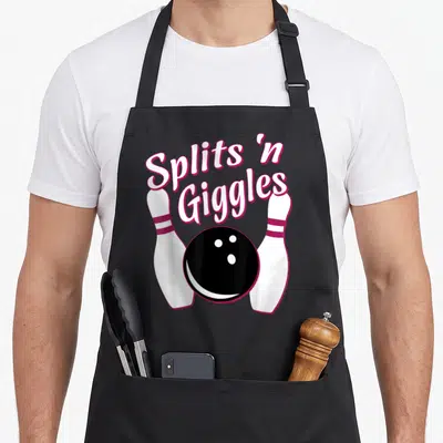 Bowling split apron - Splits n Giggles text above black bowling ball flanked by two white pins with pink outlines — shown on a black cotton canvas apron against a white background