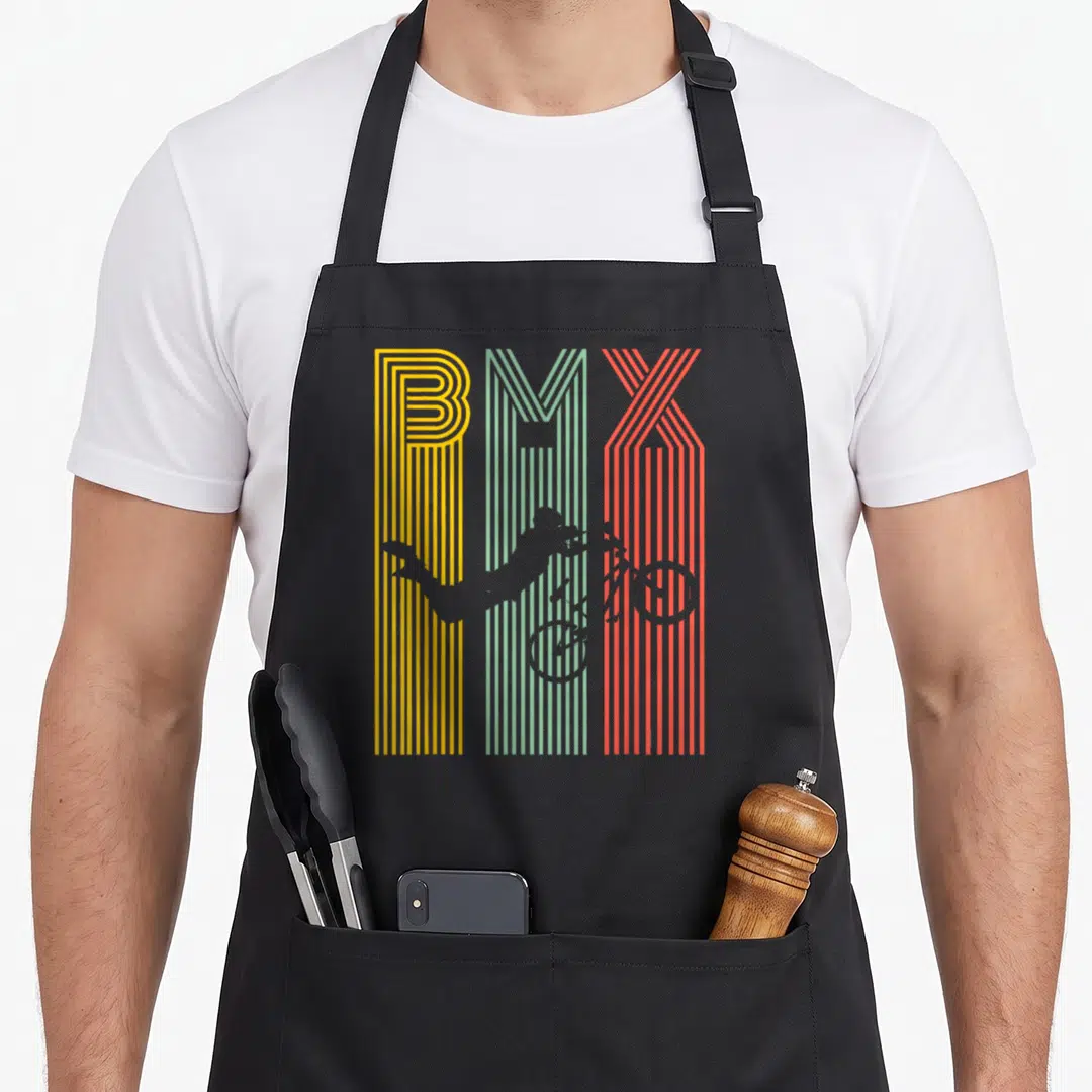 Bicycle bike apron - BMX text in yellow teal and red stripes with grey rider silhouette performing a trick — shown on a black cotton canvas apron against a white background