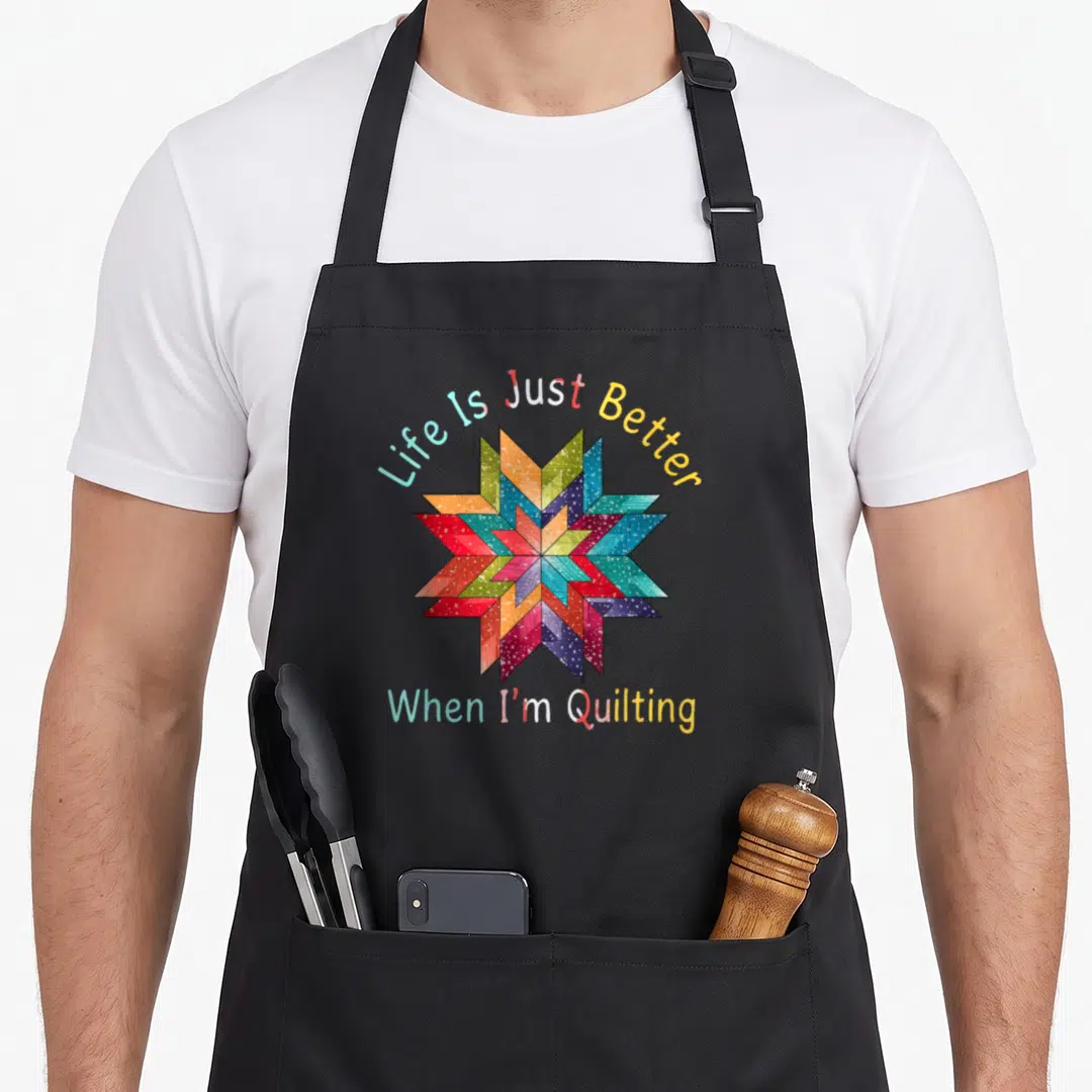Better quilter apron - Colorful quilt star with Life Is Just Better When I'm Quilting text in red blue yellow green — shown on a black cotton canvas apron against a white background