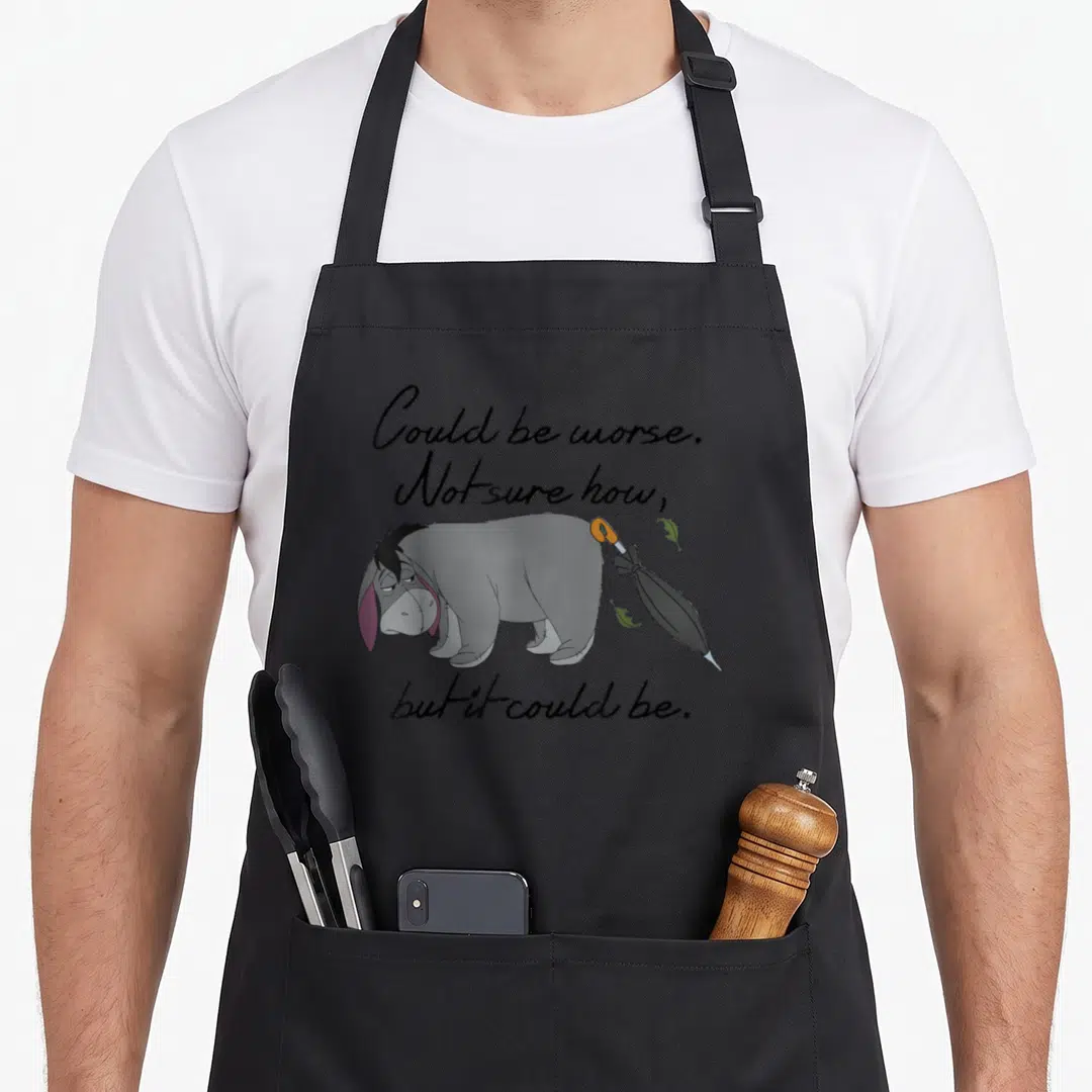 Could eeyore apron - Grey cartoon donkey with umbrella at rear and sarcastic quote text — shown on a black cotton canvas apron against a white background