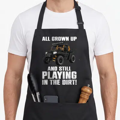 Offroad utv apron - Black UTV with orange accents flanked by white All Grown Up text blocks — shown on a black cotton canvas apron against a white background