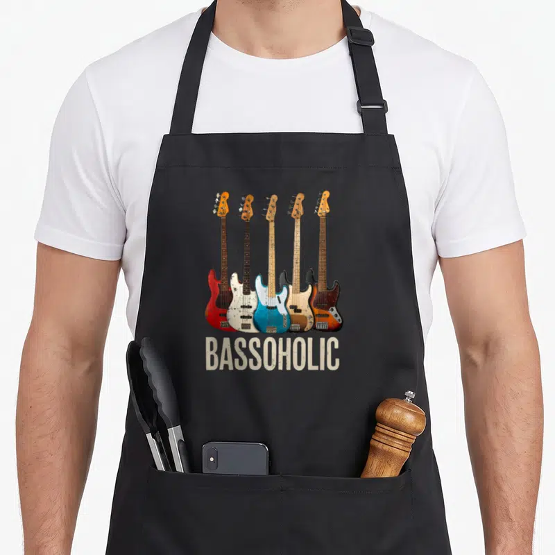 Bassoholic bassoon apron - Five bass guitars in red blue white black beige with BASSOHOLIC text below — shown on a black cotton canvas apron against a white background