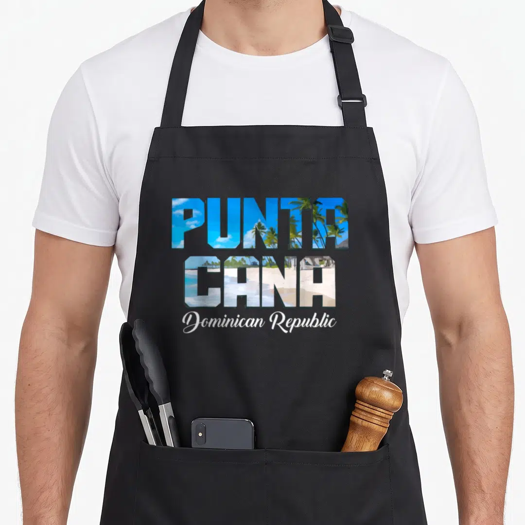 Surfer dominican boy apron - Punta Cana letters filled with beach scene and Dominican Republic script — shown on a black cotton canvas apron against a white background