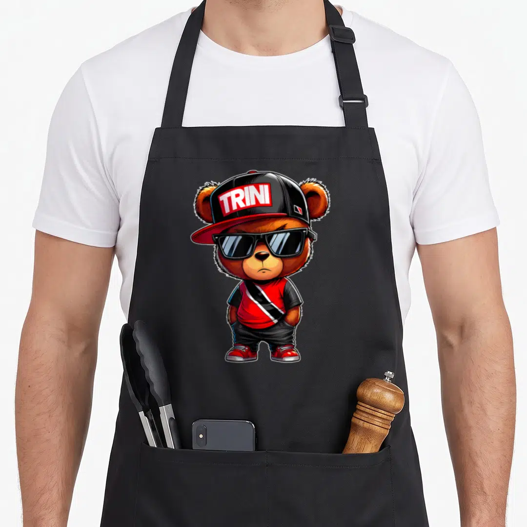 Trini teddy bear apron - Cartoon bear wearing sunglasses and cap with TRINI text in red black and white — shown on a black cotton canvas apron against a white background