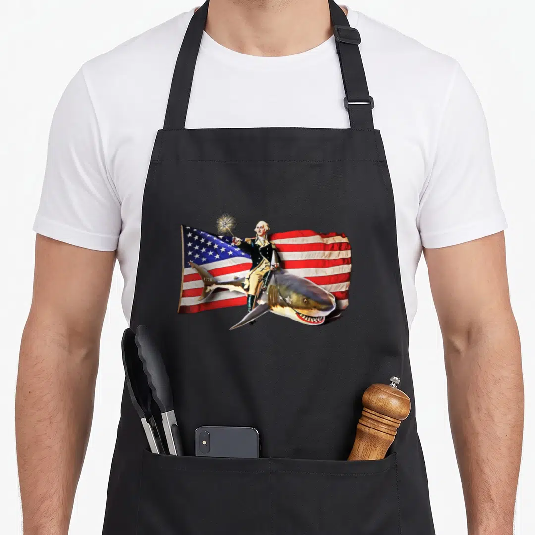 Washington 4th of july apron - George Washington riding a shark holding a sparkler with 1776 text and USA flag — shown on a black cotton canvas apron against a white background