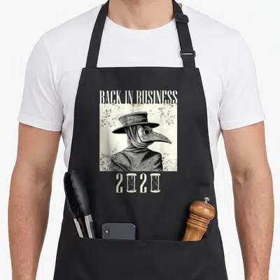 Plague business apron - Distressed plague doctor portrait with BACK IN BUSINESS text and 2020 hourglass numbers — shown on a black cotton canvas apron against a white background
