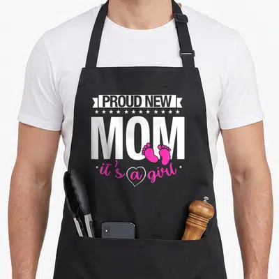 Funny proud mom apron - White PROUD NEW MOM text with pink footprints and it's a girl in a heart — shown on a black cotton canvas apron against a white background
