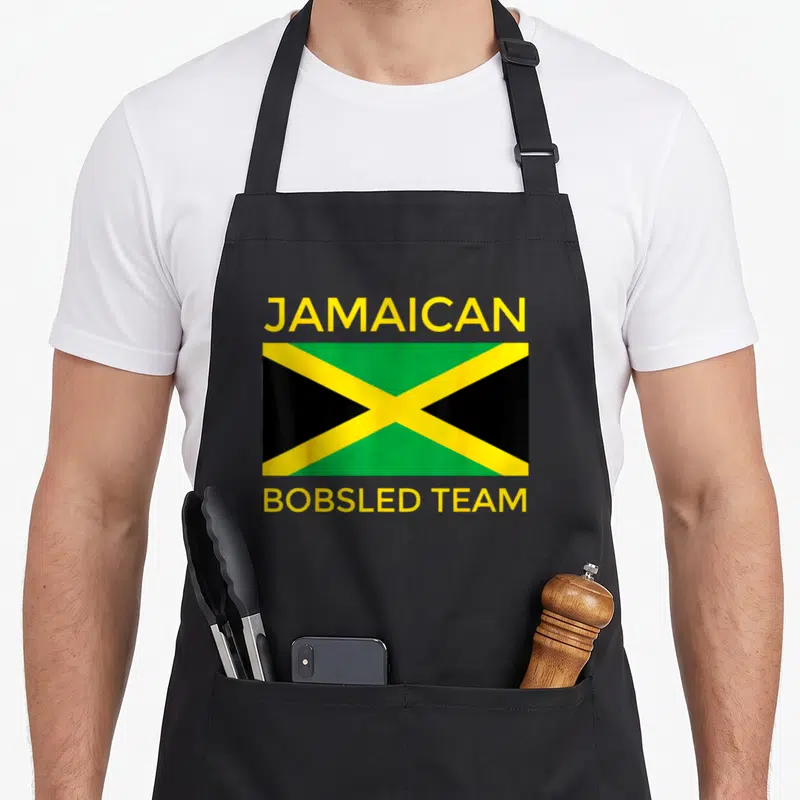 Flag bobsled apron - Jamaican flag with yellow JAMAICAN BOBSLED TEAM text in yellow green and black — shown on a black cotton canvas apron against a white background