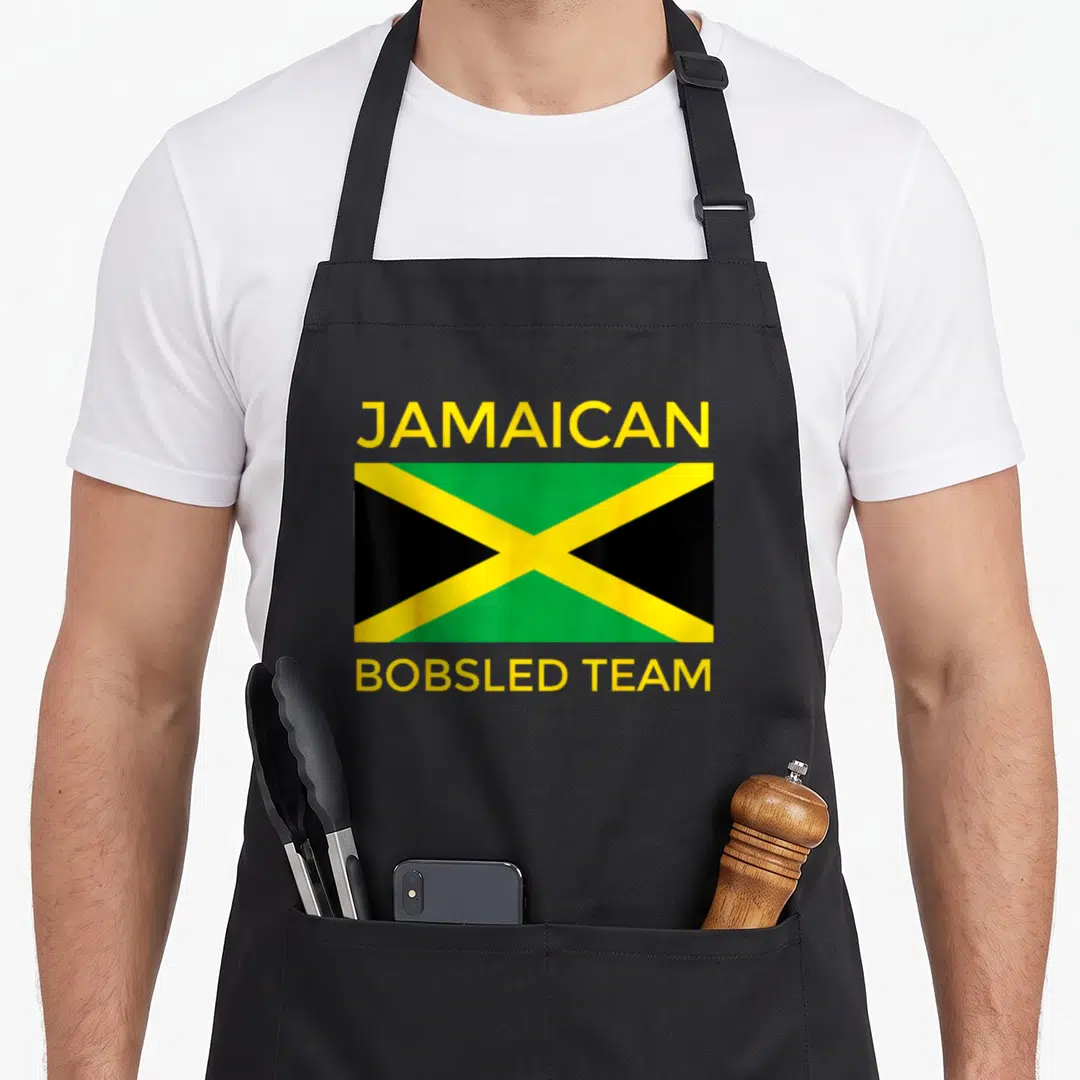 Flag bobsled apron - Jamaican flag with yellow JAMAICAN BOBSLED TEAM text in yellow green and black — shown on a black cotton canvas apron against a white background