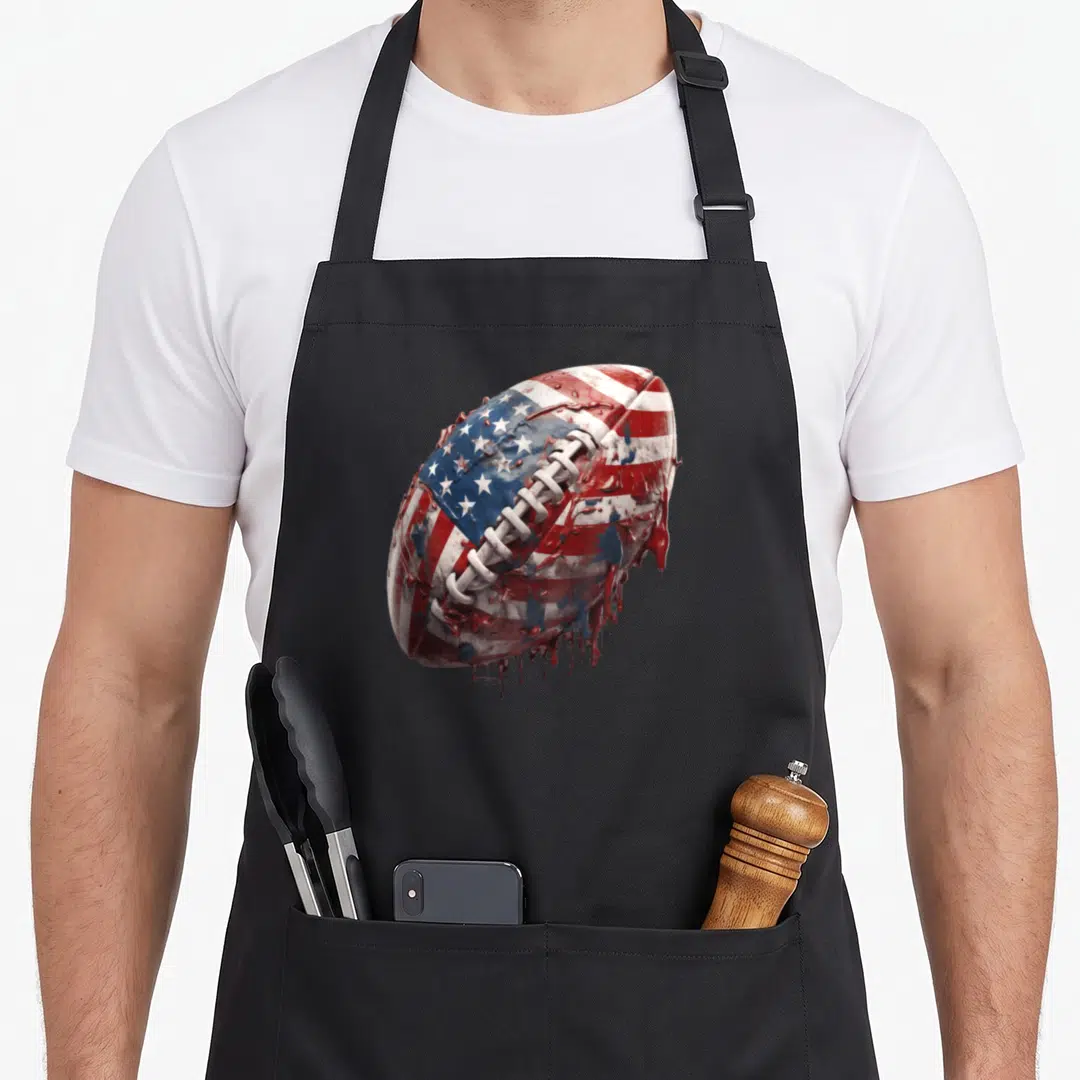 Flag football apron - Realistic football with American flag pattern and red white blue paint dripping — shown on a black cotton canvas apron against a white background