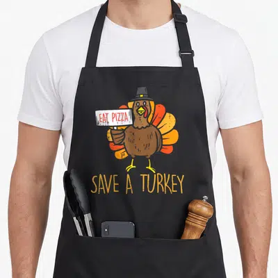 Save pizza apron - Cartoon turkey in pilgrim hat holding eat pizza sign with save a turkey text below — shown on a black cotton canvas apron against a white background