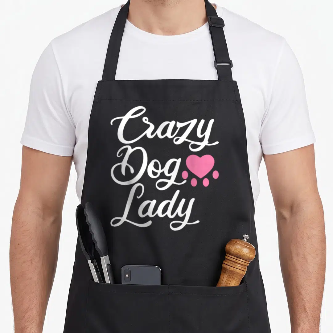 Puppy pup apron - White script text Crazy Dog Lady beside a pink heart-shaped paw print — shown on a black cotton canvas apron against a white background