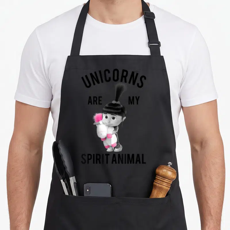 Despicable animal apron - Girl holding pink unicorn plush with text unicorns are my spirit animal — shown on a black cotton canvas apron against a white background