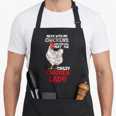 Funny animal chicken apron for grilling - Realistic grey hen with red comb surrounded by Mess With My Chickens And You — shown on a black cotton canvas apron against a white background