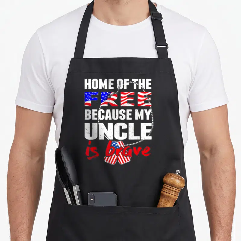 Brave niece apron - Vertical text with flag-patterned FREE, dog tag chain, two flag-filled tags forming heart at bottom — shown on a black cotton canvas apron against a white background