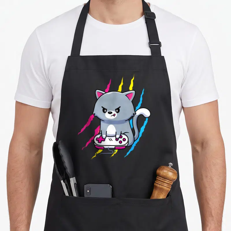 Pansexual geek apron - Grey cartoon cat sitting on a white game controller with pink, yellow, and blue lightning bolts — shown on a black cotton canvas apron against a white background