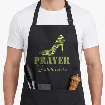 Faith prayer apron - Olive green camouflage high heel shoe above PRAYER Warrior text in tan script — shown on a black cotton canvas apron against a white background