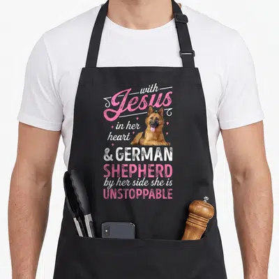 Jesus german apron - German Shepherd illustration surrounded by pink stars and stacked faith-based text — shown on a black cotton canvas apron against a white background