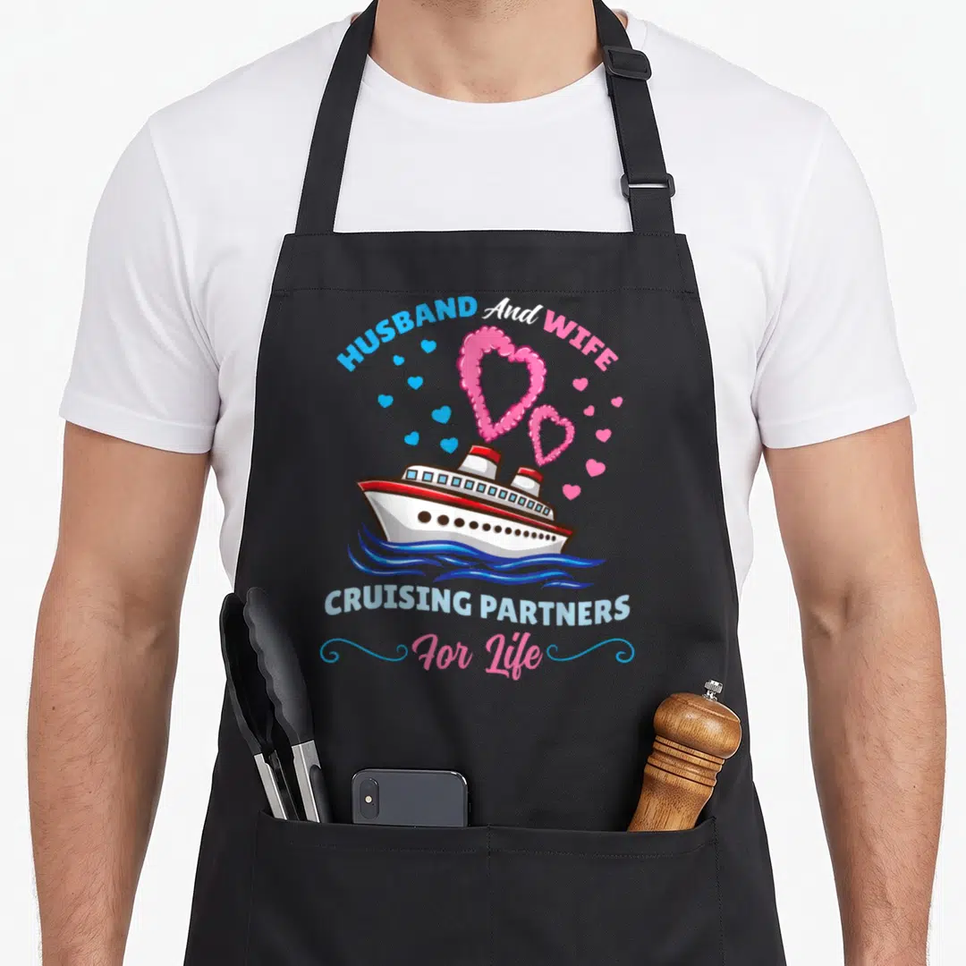 Cruising partner husband wife aprons - Cartoon cruise ship with pink hearts and blue waves under arched text — shown on a black cotton canvas apron against a white background