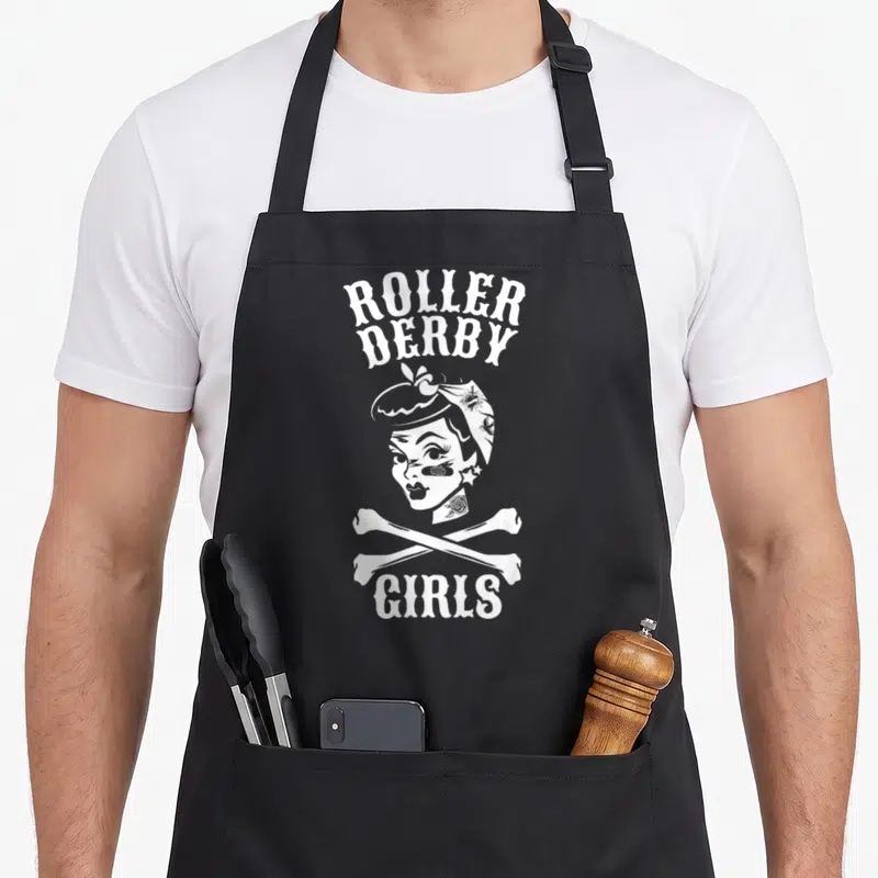 Roller pinup apron - White ROLLER DERBY GIRLS text above a tattooed woman with crossed bones — shown on a black cotton canvas apron against a white background