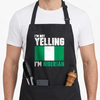 Yelling nigerian apron - Distressed text I'm Not Yelling I'm Nigerian above and below a green and white flag — shown on a black cotton canvas apron against a white background