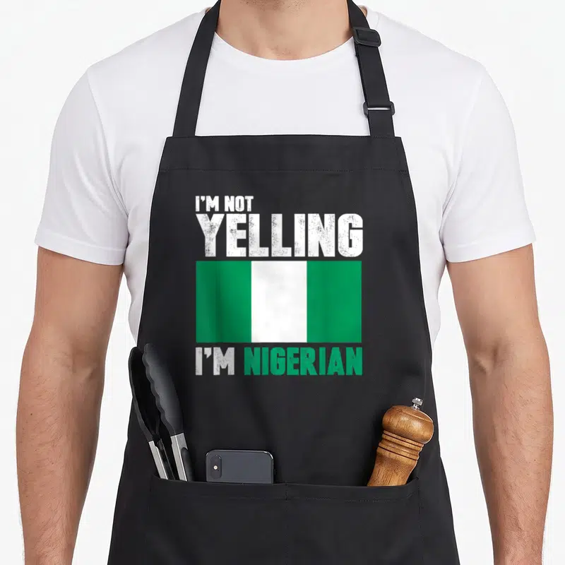 Yelling nigerian apron - Distressed text I'm Not Yelling I'm Nigerian above and below a green and white flag — shown on a black cotton canvas apron against a white background