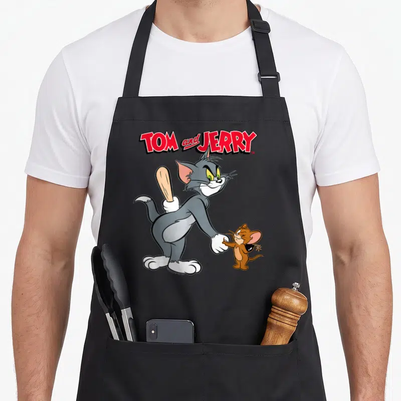 Hand crew neck apron - Tom and Jerry cartoon characters shaking hands, cat hiding a bat, mouse holding a bomb — shown on a black cotton canvas apron against a white background