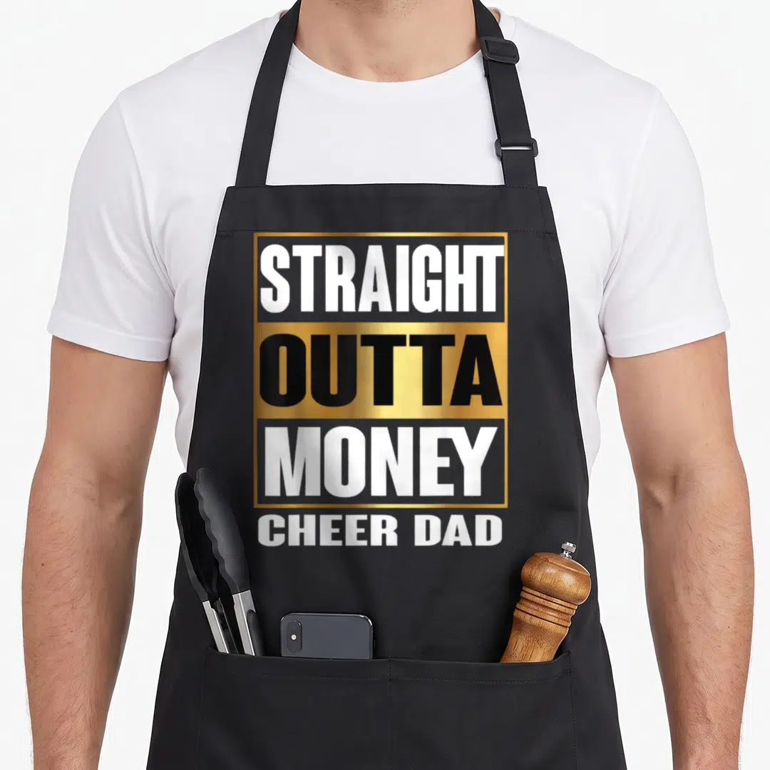 Straight outta money apron - Stacked gold and white text reading Straight Outta Money Cheer Dad on black background — shown on a black cotton canvas apron against a white background
