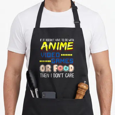 Pun video game apron - Stacked text reading anime video games or food with two donuts replacing O's in colorful — shown on a black cotton canvas apron against a white background