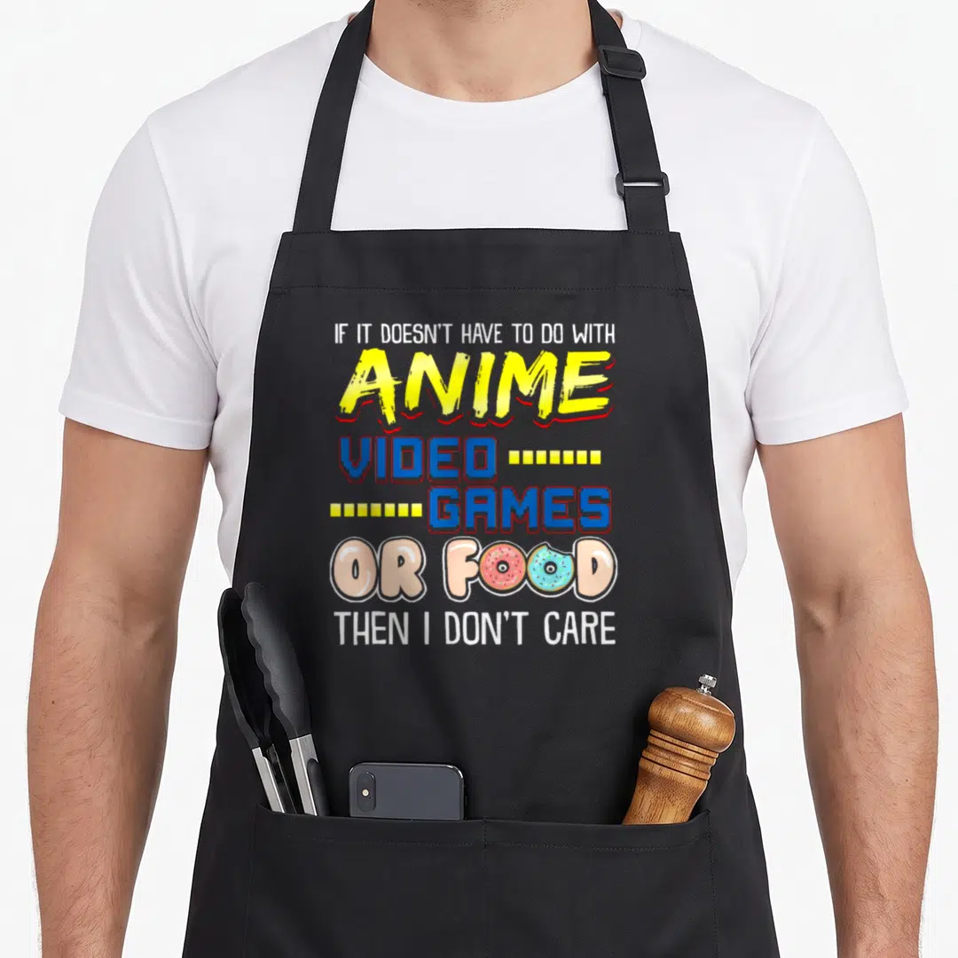 Pun video game apron - Stacked text reading anime video games or food with two donuts replacing O's in colorful — shown on a black cotton canvas apron against a white background