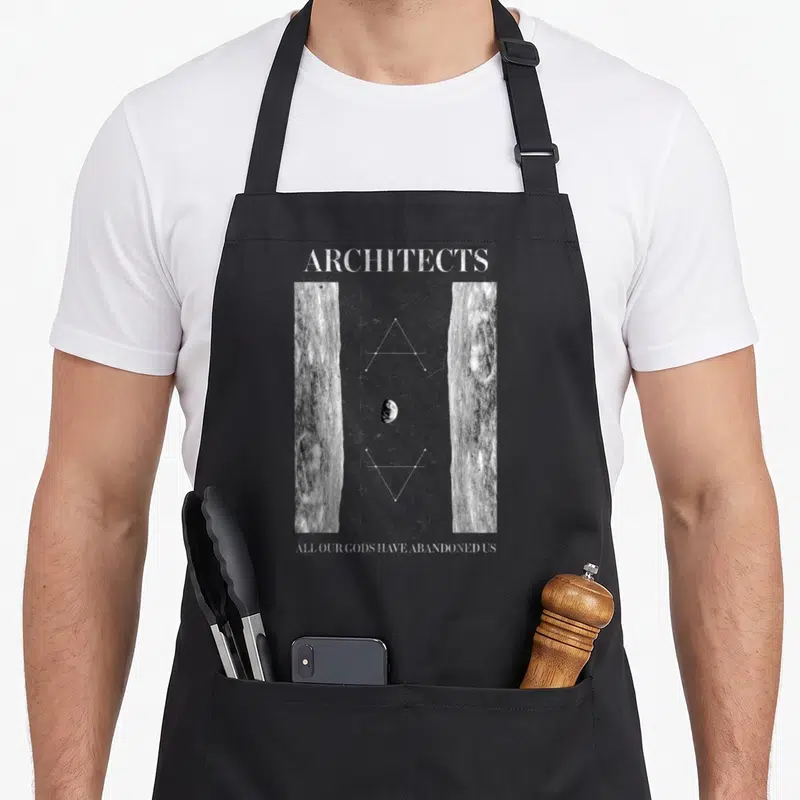Architect uk aprons - Abstract geometric design with planet, plus signs, triangles, and two vertical stone-textured — shown on a black cotton canvas apron against a white background