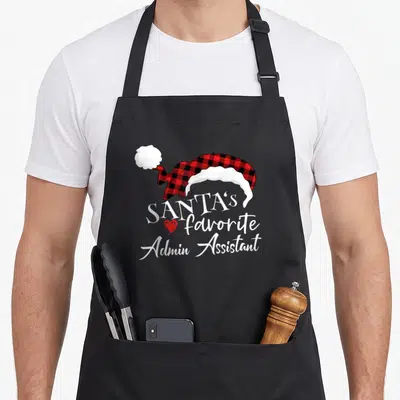 Santas administrative assistant apron - Red and black plaid Santa hat above white text reading SANTA'S favorite Admin — shown on a black cotton canvas apron against a white background