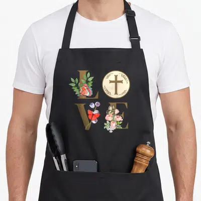 Eucharist 1st communion aprons - Watercolor LOVE text with cross circle and butterflies in tan pink green orange — shown on a black cotton canvas apron against a white background