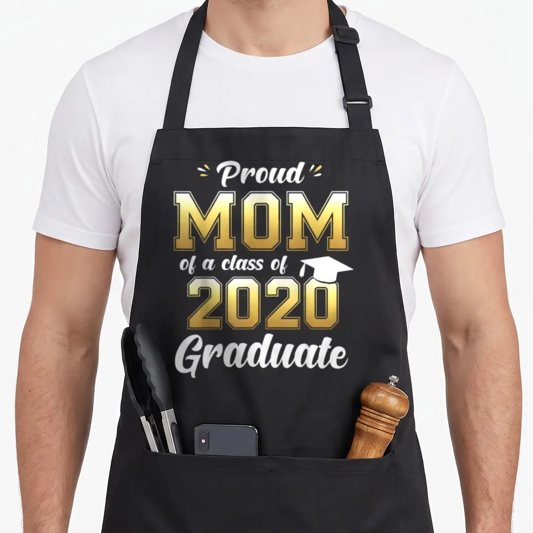 Proud graduation year apron - Stacked text Proud Mom of a class of 2020 Graduate with small white cap icon — shown on a black cotton canvas apron against a white background