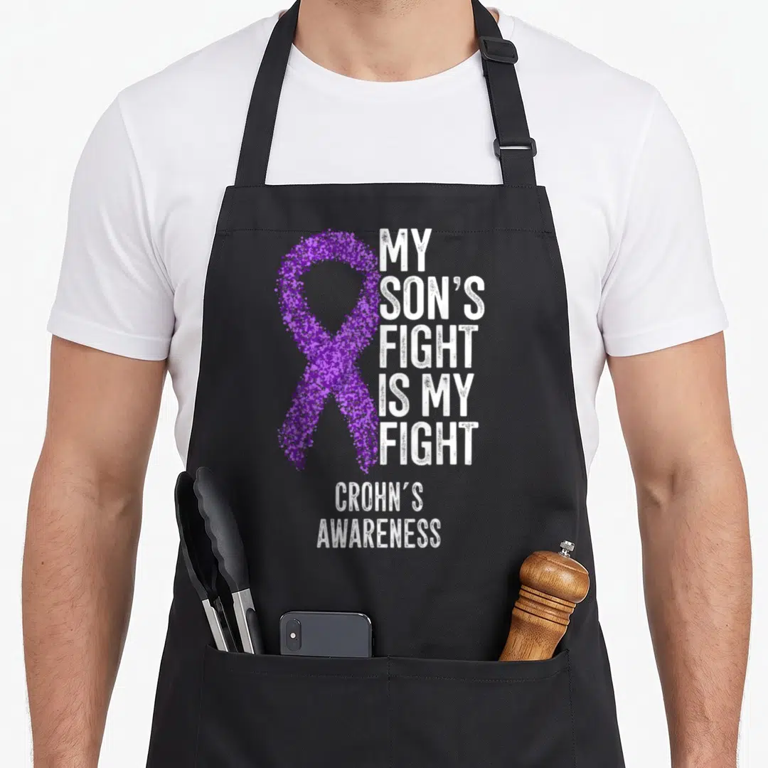 Battle crohns awareness apron - Purple dotted ribbon and white text MY SON'S FIGHT IS MY FIGHT CROHN'S AWARENESS — shown on a black cotton canvas apron against a white background