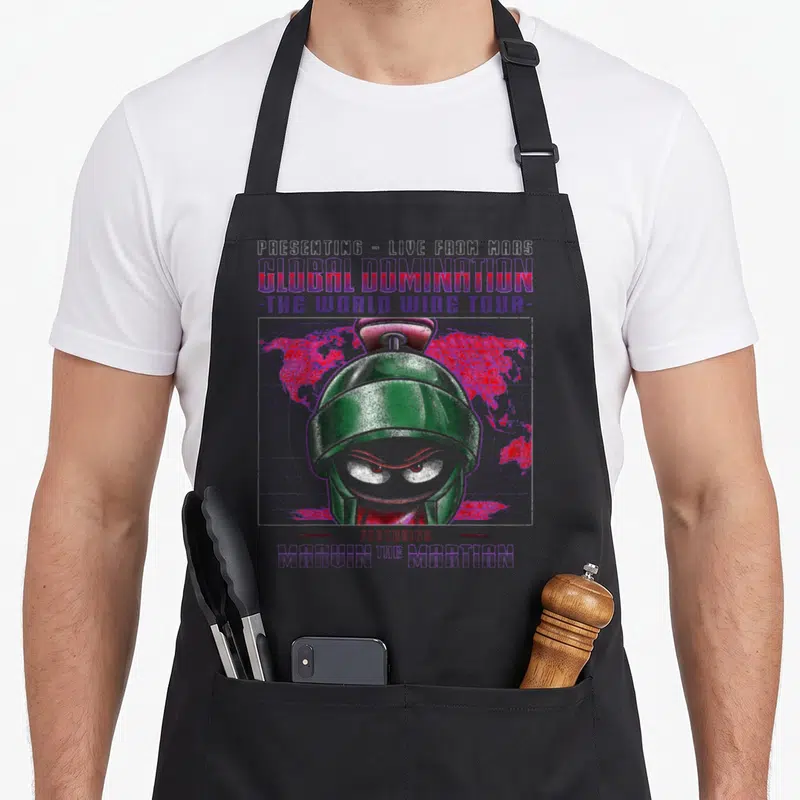 Marvin looney tune apron - Green robot head over red world map and purple grid with presenting live from mars text — shown on a black cotton canvas apron against a white background