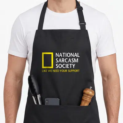 National sarcastic novelty apron - Yellow rectangular frame next to white National Sarcasm Society text and yellow — shown on a black cotton canvas apron against a white background
