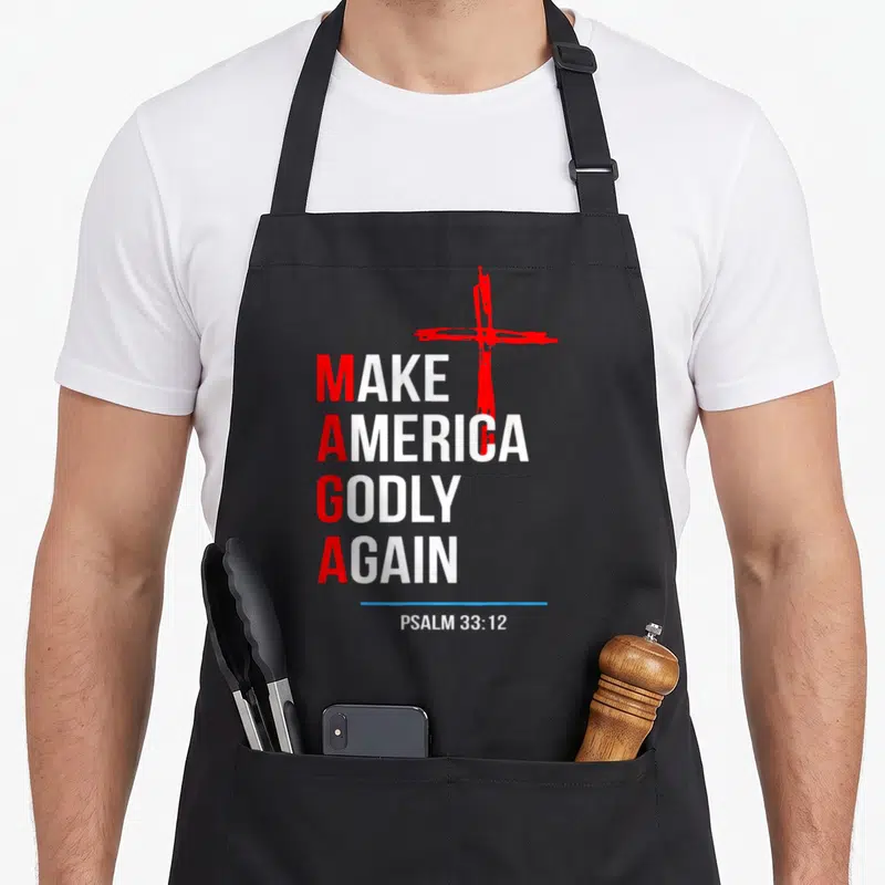 Godly hymn apron - Stacked text Make America Godly Again with red cross and Psalm 33:12 — shown on a black cotton canvas apron against a white background