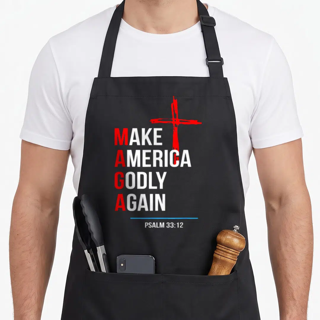 Godly hymn apron - Stacked text Make America Godly Again with red cross and Psalm 33:12 — shown on a black cotton canvas apron against a white background