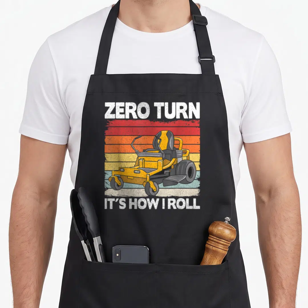 Zero hawk dad apron - Retro yellow zero turn mower on red orange striped background with white text — shown on a black cotton canvas apron against a white background