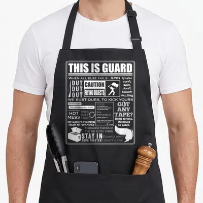 Guard meme apron - White text collage reading THIS IS GUARD CAUTION FLYING OBJECTS STAY IN YOUR TOASTER with icons — shown on a black cotton canvas apron against a white background