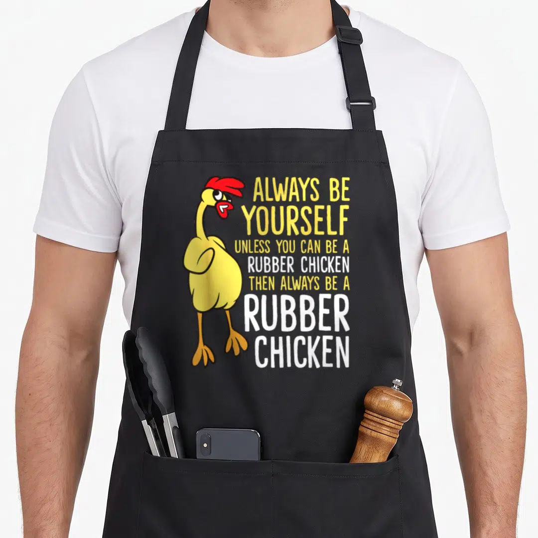 Alway chicken apron - Cartoon yellow rubber chicken with red details next to stacked yellow and white text — shown on a black cotton canvas apron against a white background