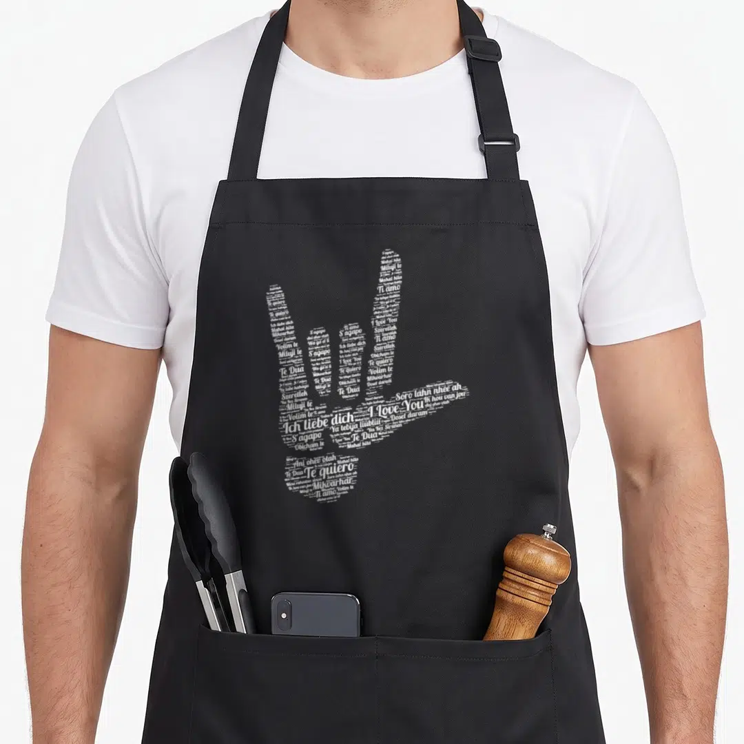 Different asl sign for apron - White text forming ASL hand sign for love with multilingual phrases — shown on a black cotton canvas apron against a white background